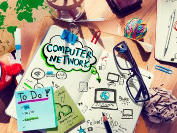 A cluttered desk with computer network notes and glasses.