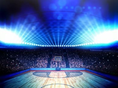 Empty basketball court illuminated by bright blue stadium lights.