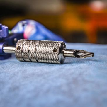Close-up of a metallic tattoo machine part on blue cloth.
