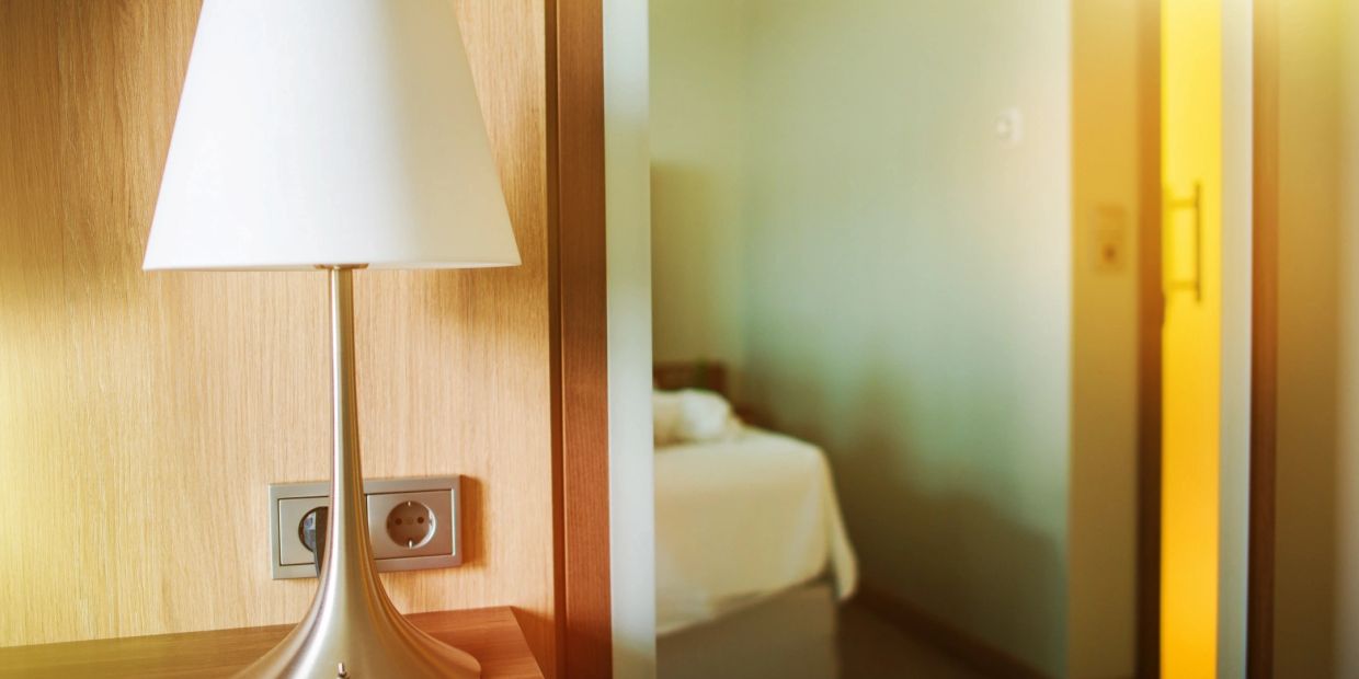 Modern lamp on wooden bedside table with blurred bedroom background.