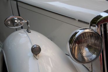 Close-up of a white classic car's front section with headlights and mirror.