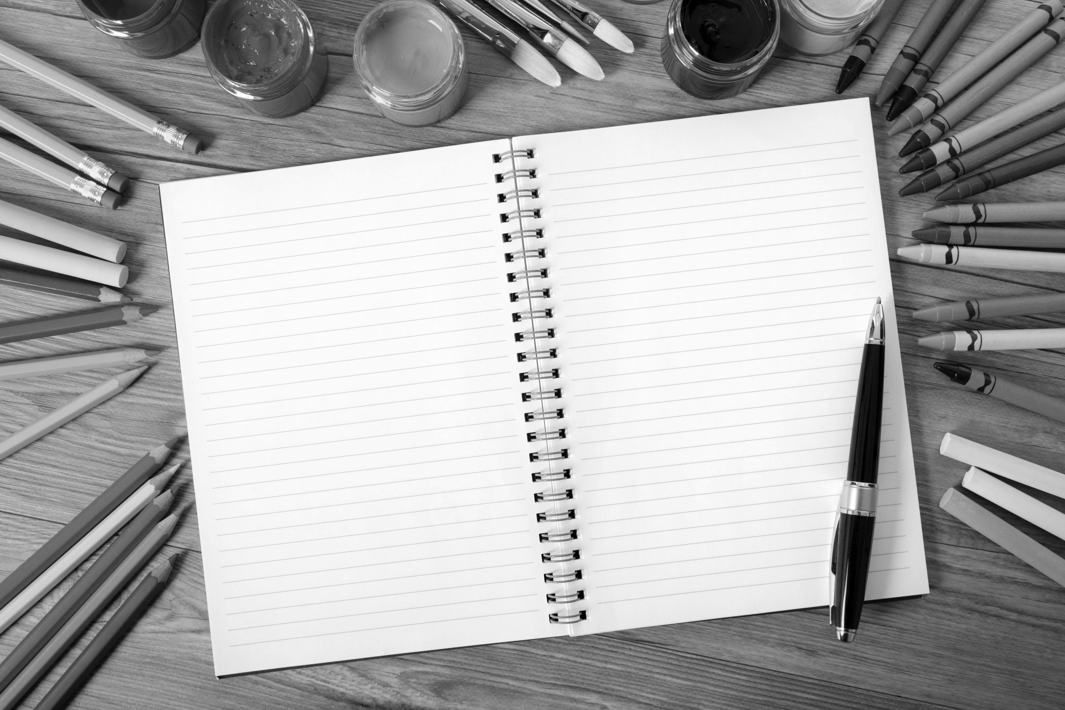 Open notebook surrounded by art supplies on wooden table.