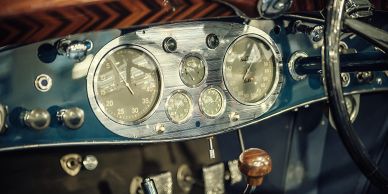 Close-up of a vintage car's dashboard with classic gauges and wooden gear shift.