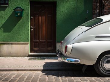 Rear view of a classic white car parked beside a green wall with a wooden door.