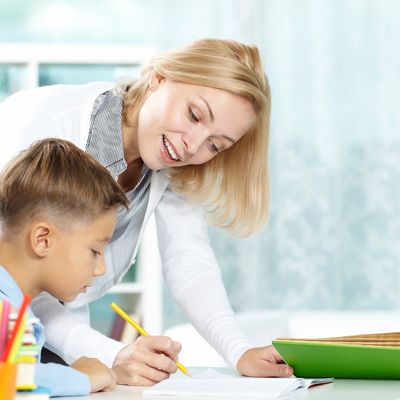 A teacher helping a young boy with his homework at a desk.