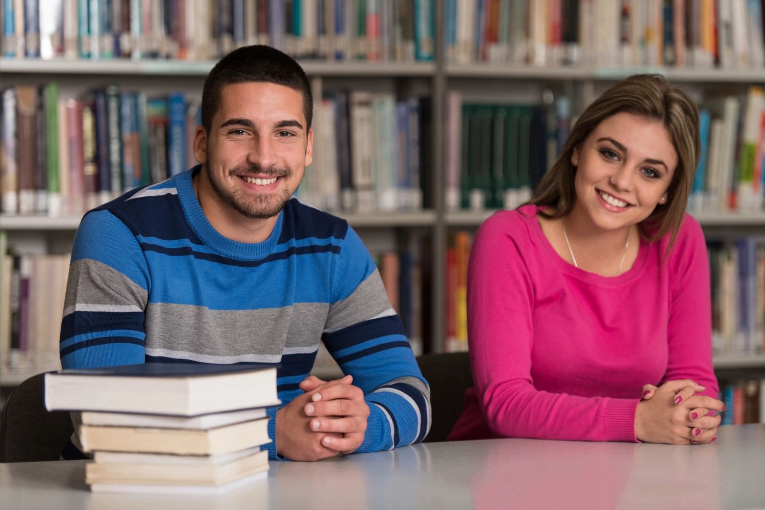 young adult students at a library studying and smiling at the camera