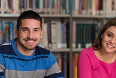 Two students smiling in a library with bookshelves behind them.