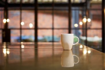 White coffee mug on a reflective wooden table.