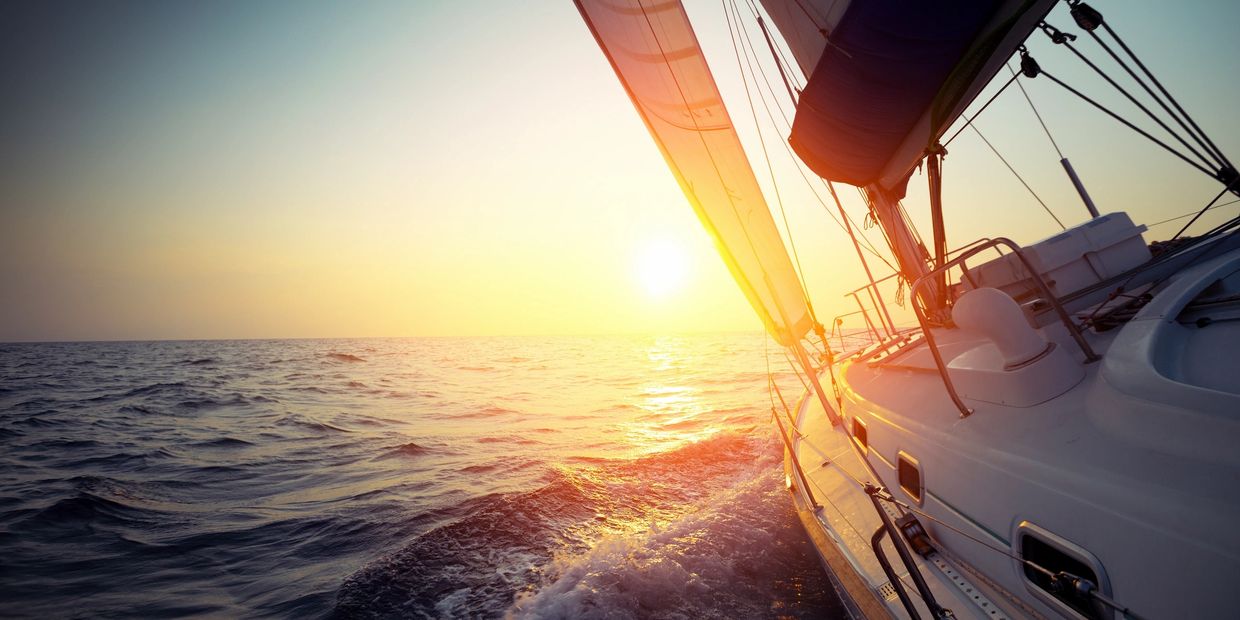 a view from the helm of the bow of a sailboat turning through waves at sunset