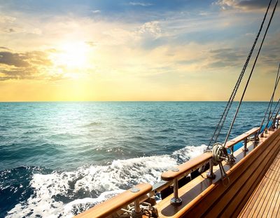 View from a wooden sailboat deck at sunset over the ocean.