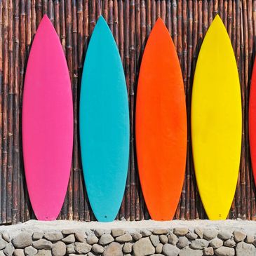 Five colorful surfboards lined up against a bamboo wall with stones below.