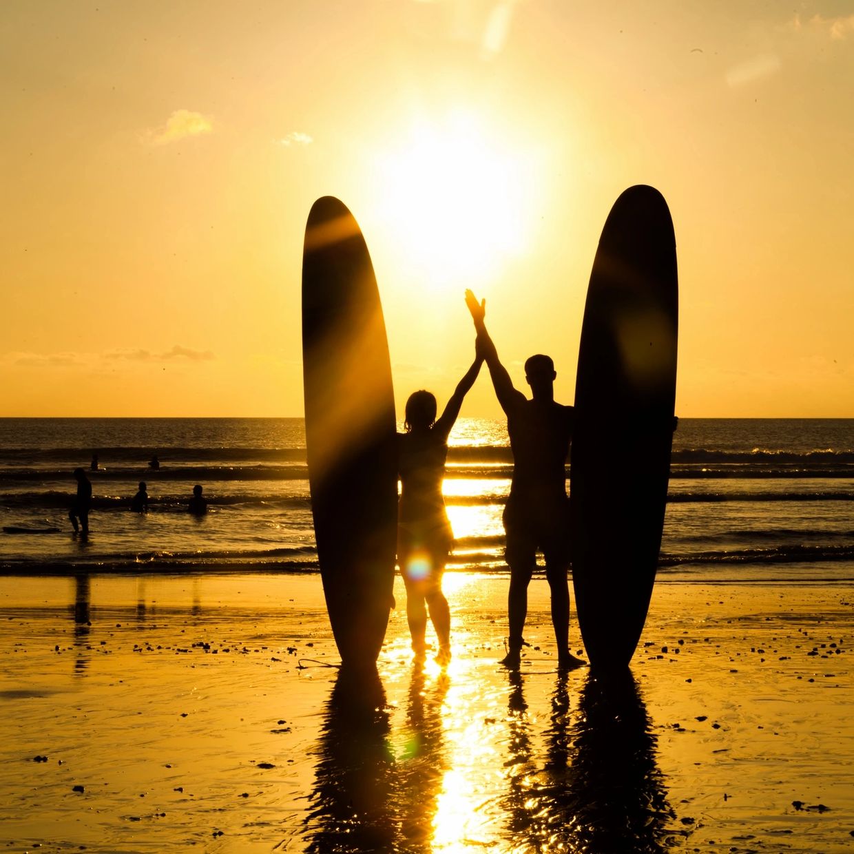 Two surfers holding boards watching the sunset.