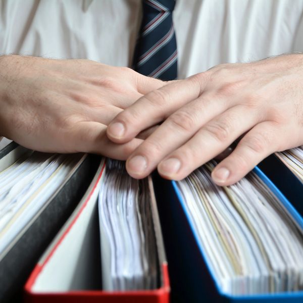 Hands resting on a stack of thick binders filled with documents.