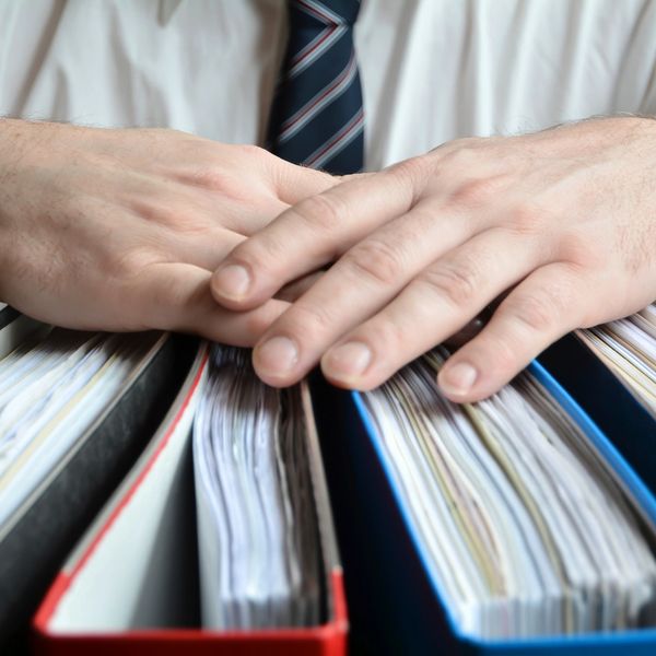 Hands resting on a stack of thick binders filled with documents.