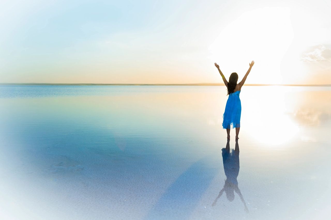 A person enjoys her wins in the sunset with her hands up.