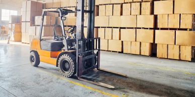 Forklift in a warehouse with stacked boxes.