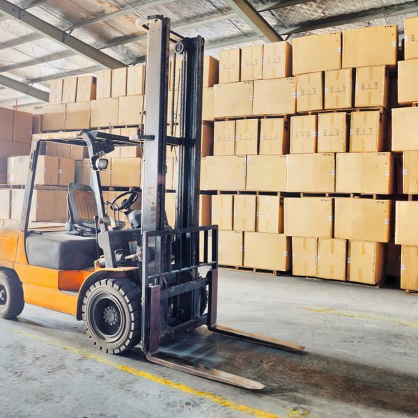 An orange forklift in a warehouse with stacked cardboard boxes.