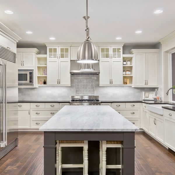 Bright white kitchen with marble island and modern stainless steel appliances.