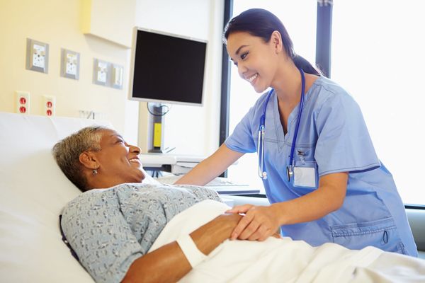 Nurse smiling and holding hands with a patient in hospital bed.