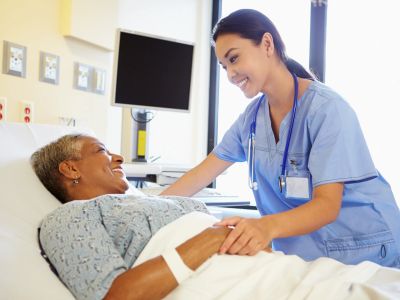Nurse smiling and holding patient's hand in hospital bed.