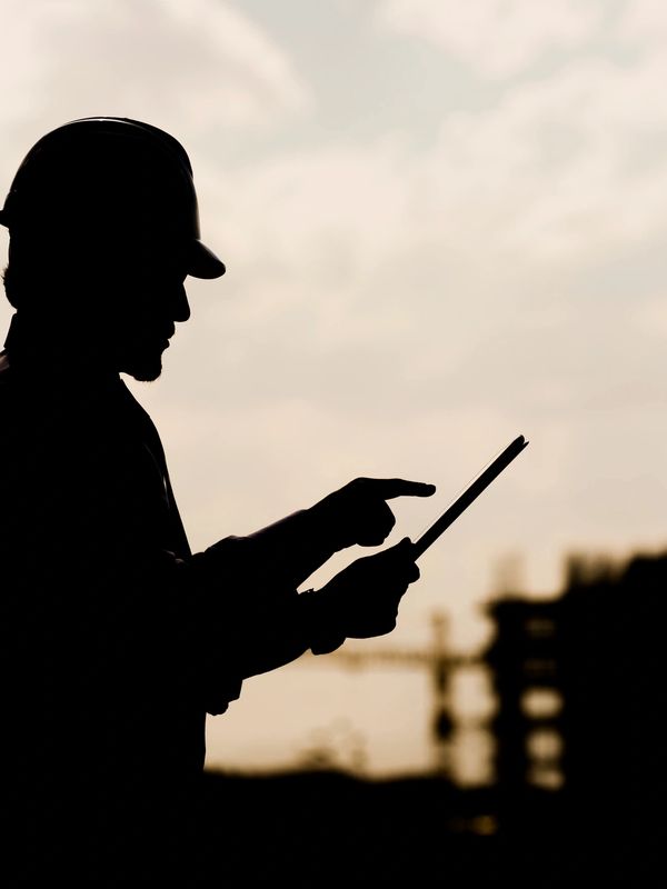 Silhouette of a construction worker using a tablet at a site.