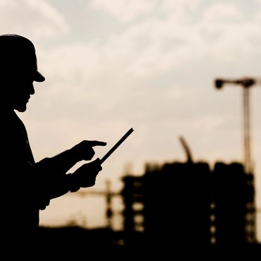 Shadowy silhouette of Special Deputy Inspector reviewing digital plans ob a tablet with high rise an