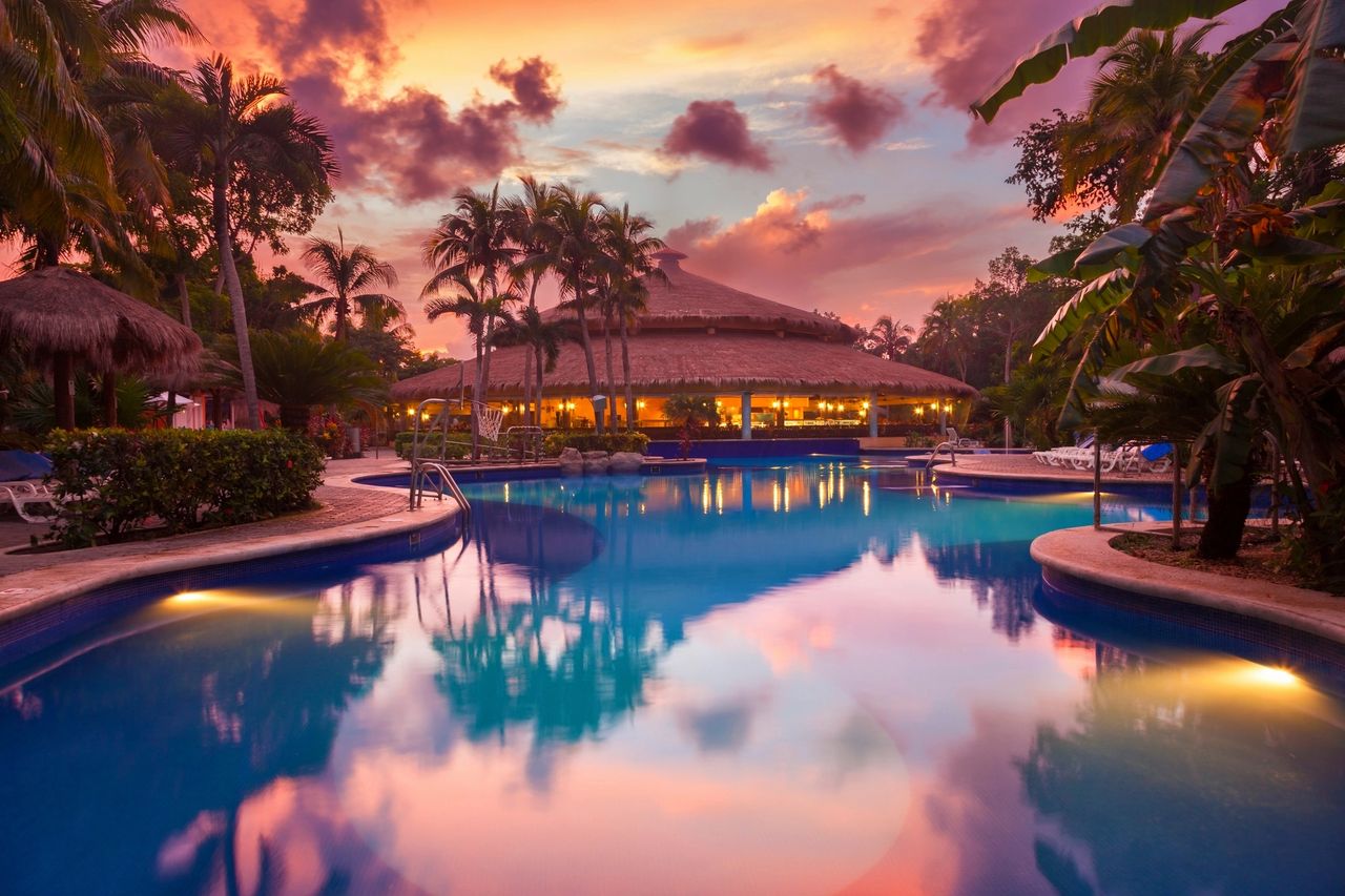 Tropical Caribbean resort pool at sunset surrounded by palm trees, with no people present, representing calm conditions and flexible travel timing in the Caribbean.