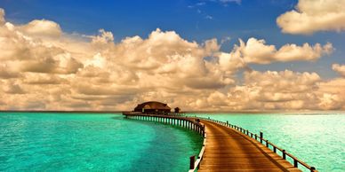 Wooden boardwalk over turquoise water leading to an overwater villa in the Maldives.