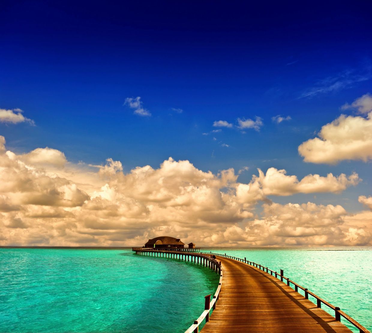 A serene pier extends into turquoise waters under a dramatic cloudy sky.