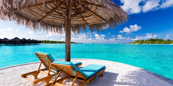 Beach chairs on a island under a straw umbrella.