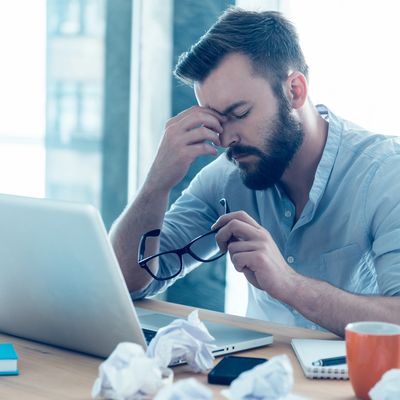 Stressed man holding glasses, rubbing eyes at his desk with crumpled papers.