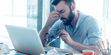 man pinching bridge of nose while sitting at laptop