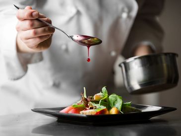 Chef delicately drizzling sauce over a fresh salad.