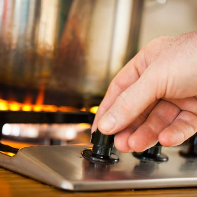 Hand adjusting stove knob with flame burning in the background.