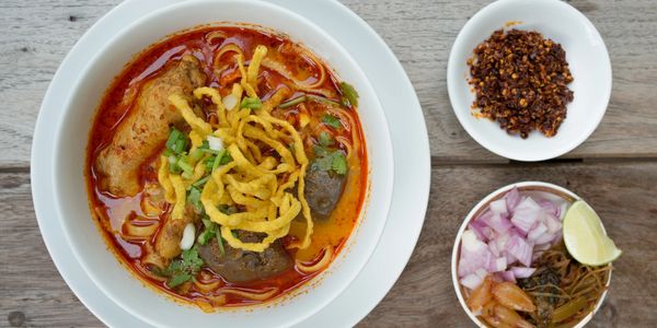 Overhead view of a bowl of khao soi served with a bowl of chili paste and a bowl of vegetables