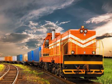 An orange freight train traveling on curved tracks under a dramatic sky.