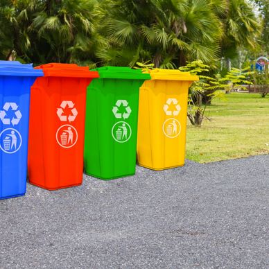 Colorful recycling bins lined up outdoors on a paved area.
