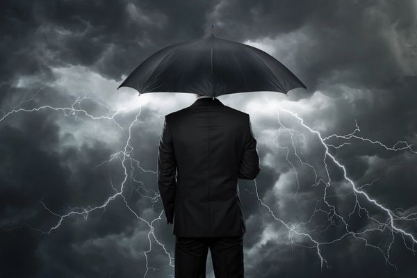 Man in suit holding umbrella under a stormy sky with lightning.