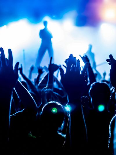 Crowd enjoying a live concert with hands raised under blue stage lights.