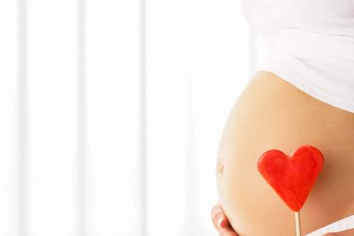 Pregnant belly with a red heart decoration symbolizing love.