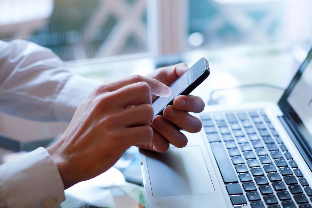 Person using a smartphone with a laptop in the background.