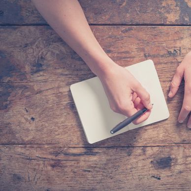 Hands poised to write on a blank notebook on a wooden table.