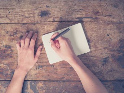 Hand holding pen over a blank journal set atop an old wood table