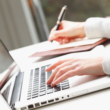 Picture of someone typing into a laptop and making notes in a note book making a plan 