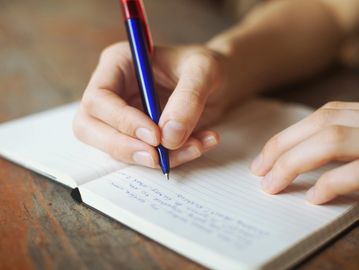 A female hand holding a pen and writing in a journal