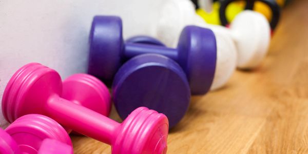 Colorful dumbbells and kettlebells lined up on a wooden floor.