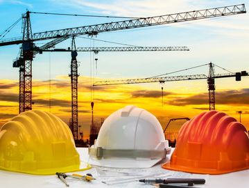 Three construction helmets with cranes and sunset in the background.