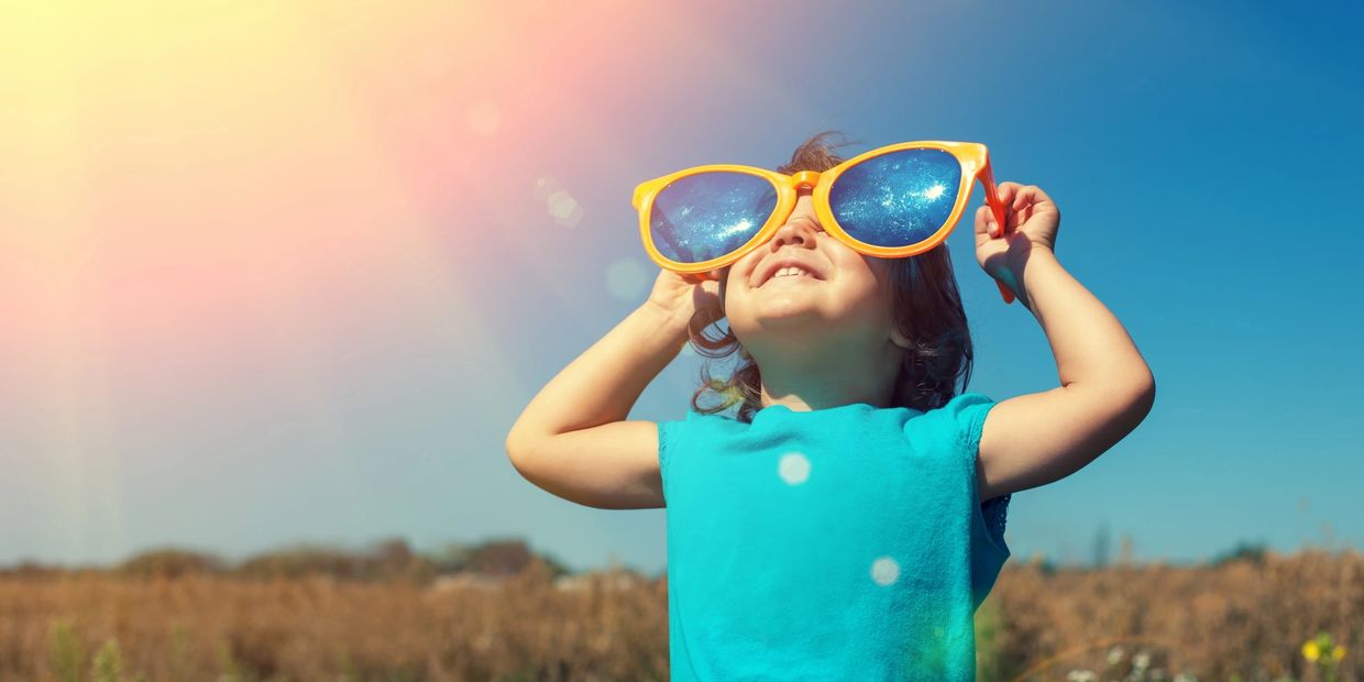Child wearing oversized sunglasses reflecting a starry sky, enjoying a sunny day outdoors.