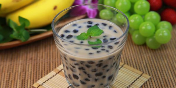 A glass of bubble tea with tapioca pearls and mint garnish.
