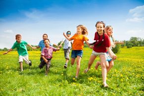 Group of children joyfully running through a green field on a sunny day.